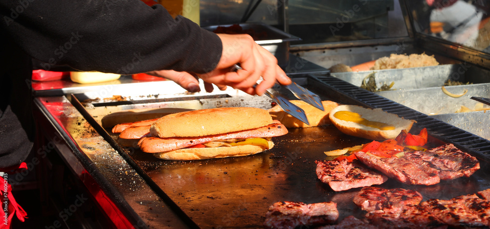 Fototapeta premium hands of cook at counter of a street food truck preparing sandwiches filled with grilled sausage and peppers