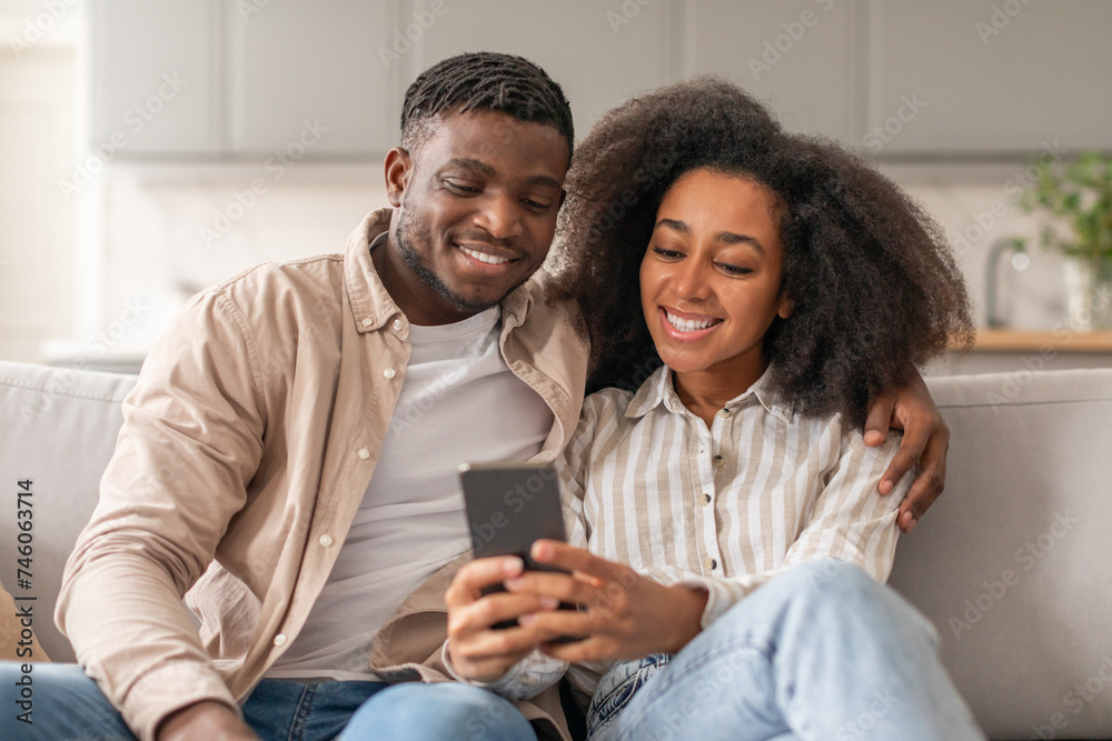 Black millennial spouses enjoying leisure time using cellphone at home Black millennial spouses enjoying leisure time using cellphone at home
