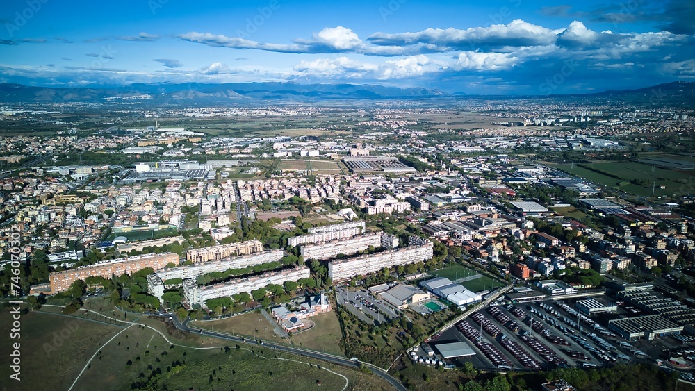 This aerial view showcases a city nestled amidst towering mountains in the background. The cityscape is dotted with buildings, roads, and green spaces, while the majestic mountains provide a stunning