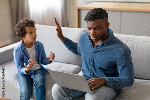 Black boy gesturing to distracted father on laptop photo