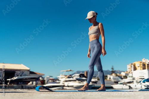 People, sport and recreation concept. a fitness woman with a perfect figure stands on a mat. a girl in sports leggings, a top and a cap stands on a fitness mat.