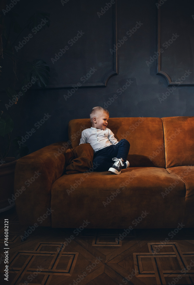 Adorable Rich Little Cute Boy on Vintage Sofa in Dark Interior