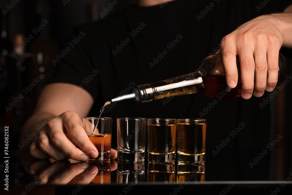 Bartender pouring alcohol drink into shot glass at mirror bar counter, closeup