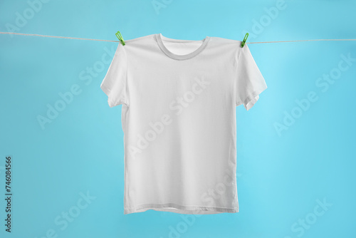 One white t-shirt drying on washing line against light blue background