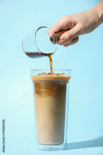 Woman making iced coffee on light blue background, closeup