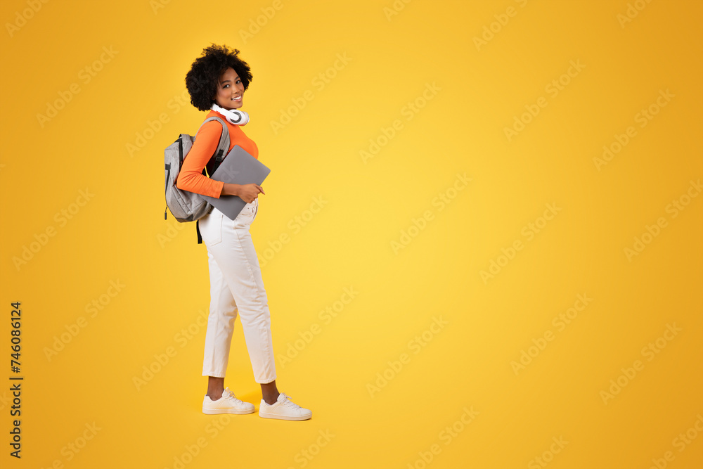 Fototapeta premium Confident young student in a vibrant orange turtleneck and white pants looks back with a smile