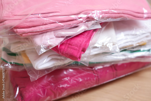 Stack of folded clothes in plastic bags on table, closeup