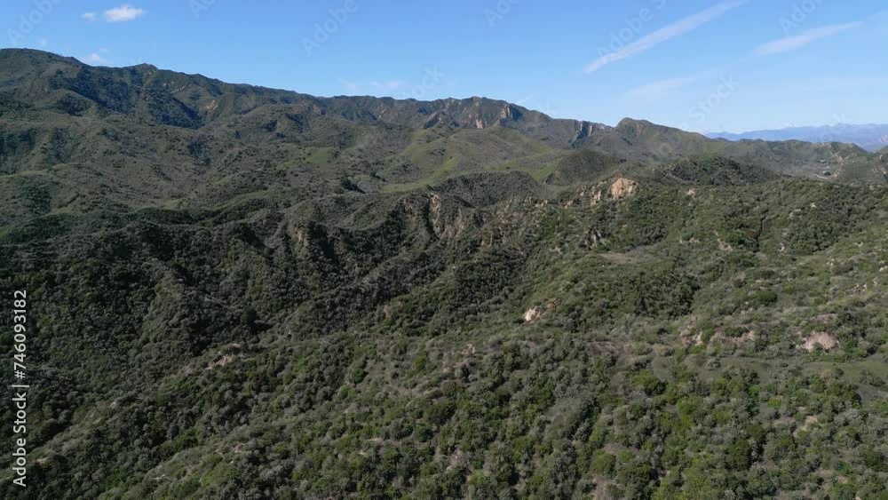 Rugged mountains with green foliage are shown in an aerial, approaching view with a blue sky during a sunny day. Rugged mountains with green foliage are shown in an aerial, approaching view with a blue sky during a sunny day.