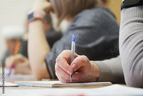 An adult woman with a fountain pen sits next to colleagues and writes in a notebook during a meeting or professional development training session.Photo. No face. Selective focus photo