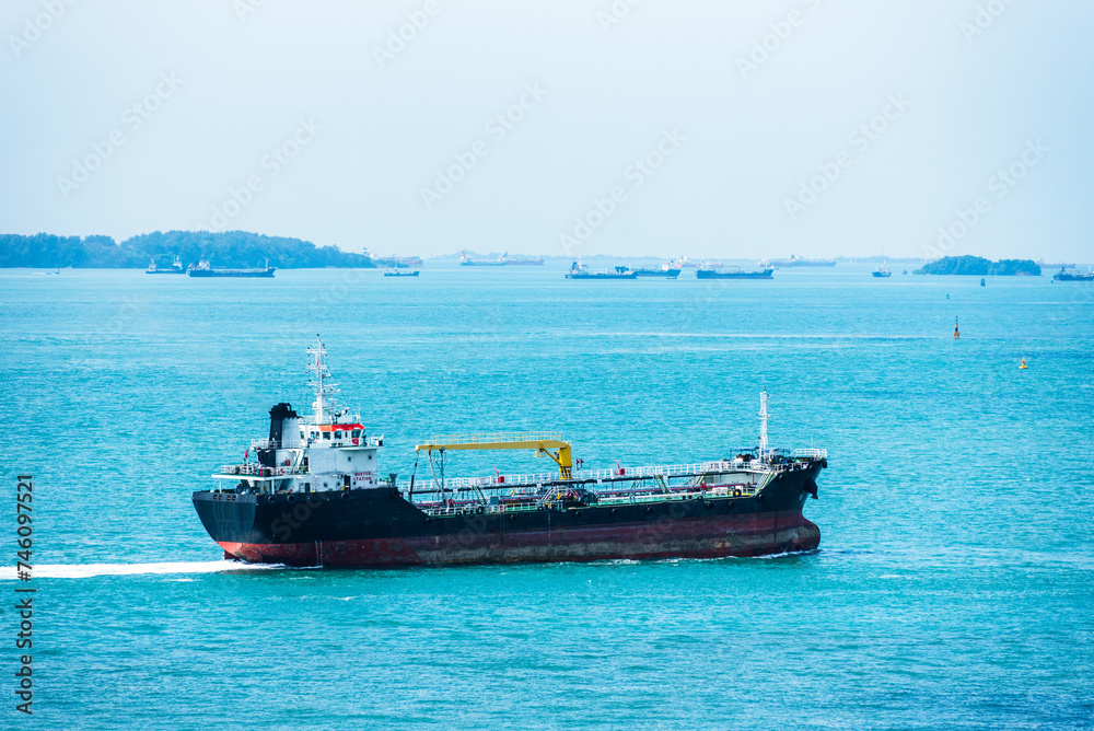 Oil tanker ship sailing through calm, blue waters inside sea port in Singapore.