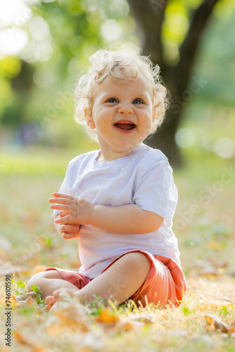 Cute curly blond baby sitting on the grass in autumn