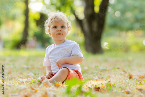 Cute curly blond baby sitting on the grass in autumn