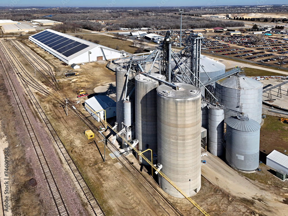 View of grain storage bins from the air with solar powered grain storage building in the background View of grain storage bins from the air with solar powered grain storage building in the background