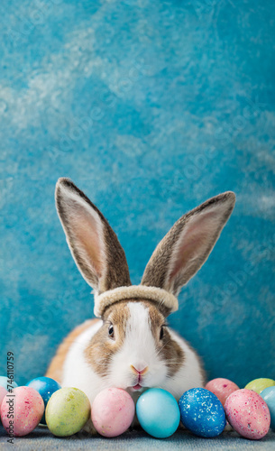 Easter poster background with copy space on top. Adorable bunny with Easter eggs on blue background. Greeting card for Easter