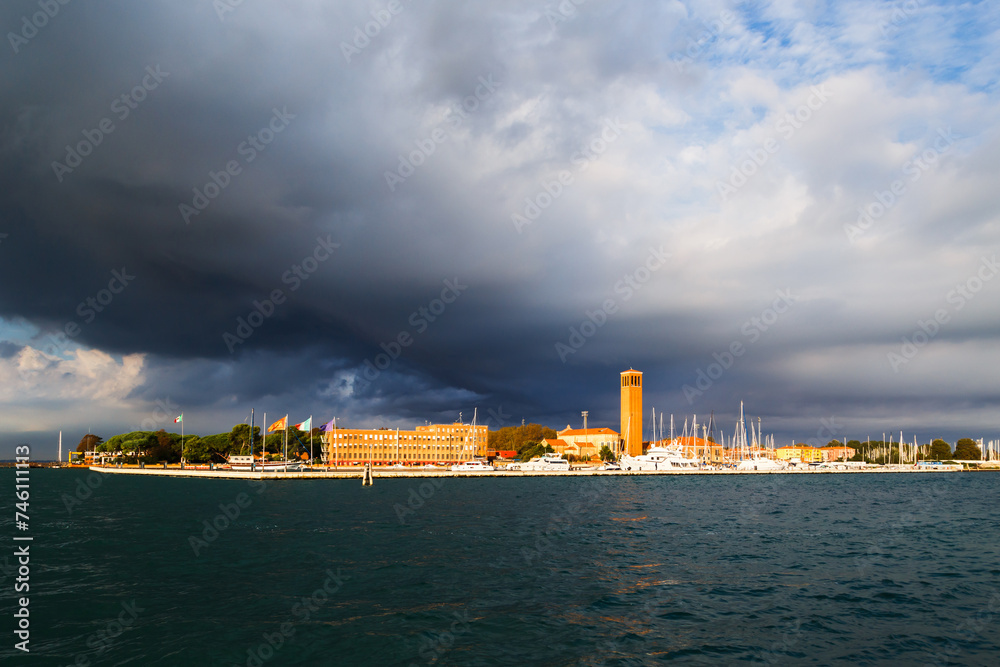 Bell tower of Sant'Elena Church and yacht harbor at extreme east end of sestiere of Castello in Venice, Italy. View from Venetian lagoon in stormy weather with dark cloudy sky in background