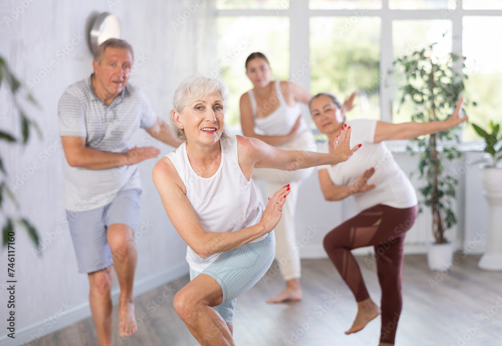 Obraz premium Group session of modern fitness for amateurs in studio. Mature lady with senior class s visitor actively moves and learns to dance balboa