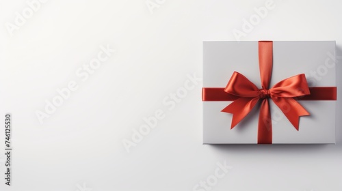 Minimalistic white gift box tied with a red ribbon on a plain backdrop. Perfect present packaging with a bow for special occasions. © Irina.Pl
