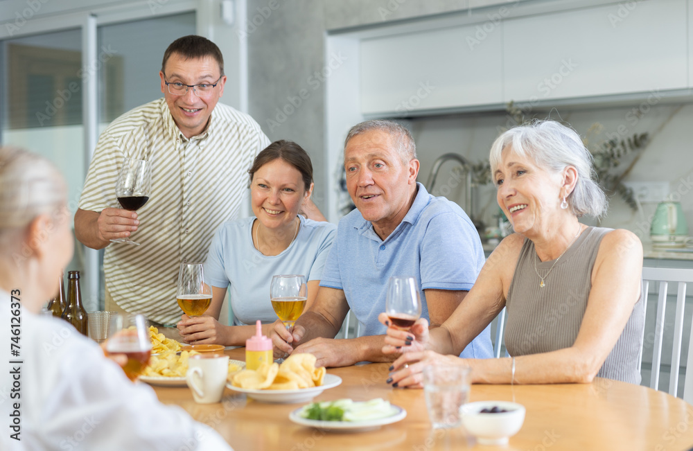Happy elderly people speaking to each other with enthusiasm while drinking and eating in the kitchen