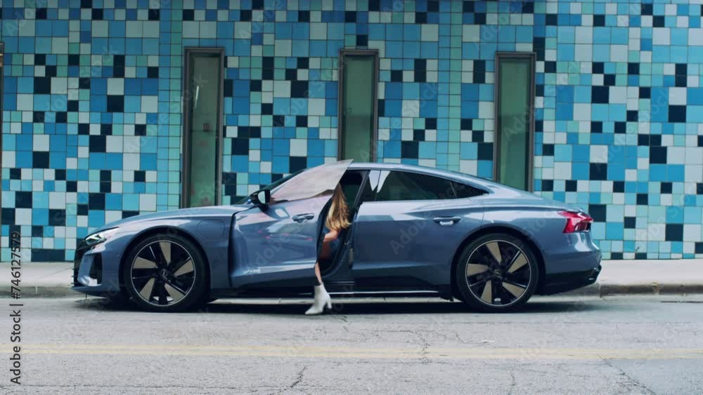 Blonde woman gets into a luxury sports car on a blue tile background