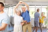 Group of elderly pensioners learn to dance a couple tango dance in a dance class