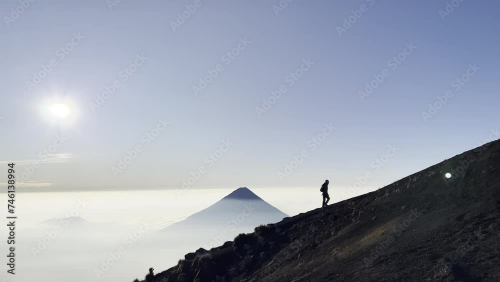Hiking with a silhouette of a hiker against the backdrop of a volcano towering over the clouds in the background. Voldaco de Fuego , Acatenango antigua Guatemala