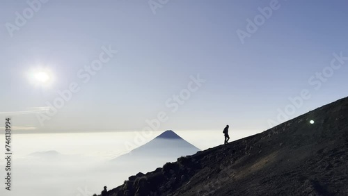 Hiking with a silhouette of a hiker against the backdrop of a volcano towering over the clouds in the background. Voldaco de Fuego , Acatenango antigua Guatemala