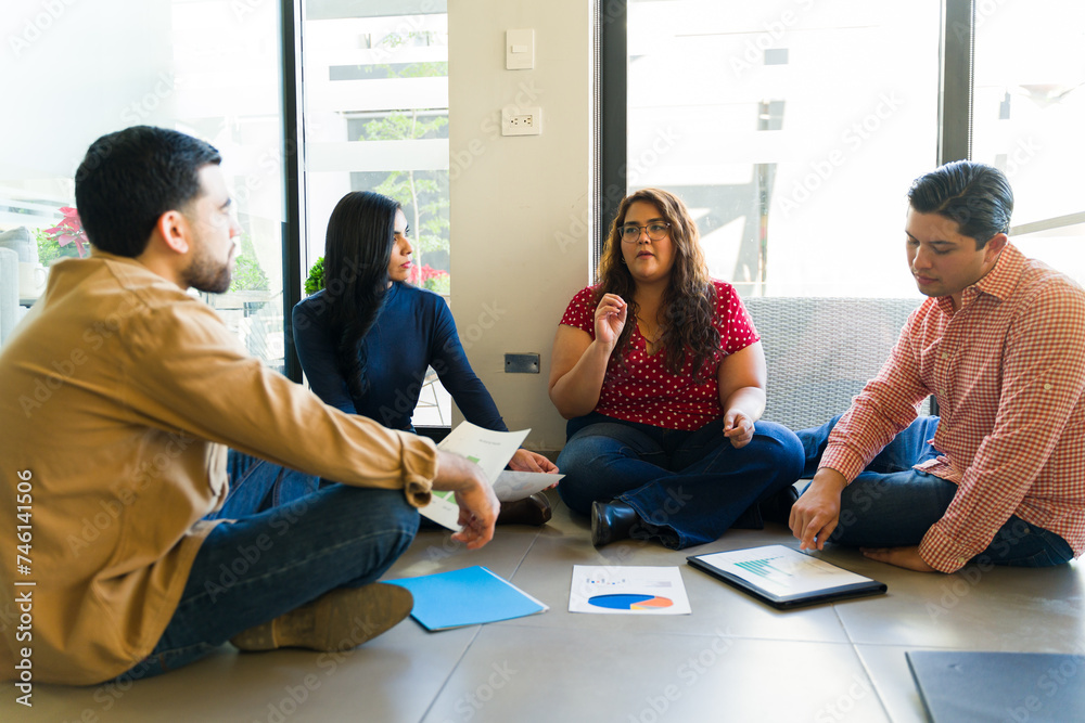 Group of four businesspeople sitting in the floor while having a casual team meeting Group of four businesspeople sitting in the floor while having a casual team meeting