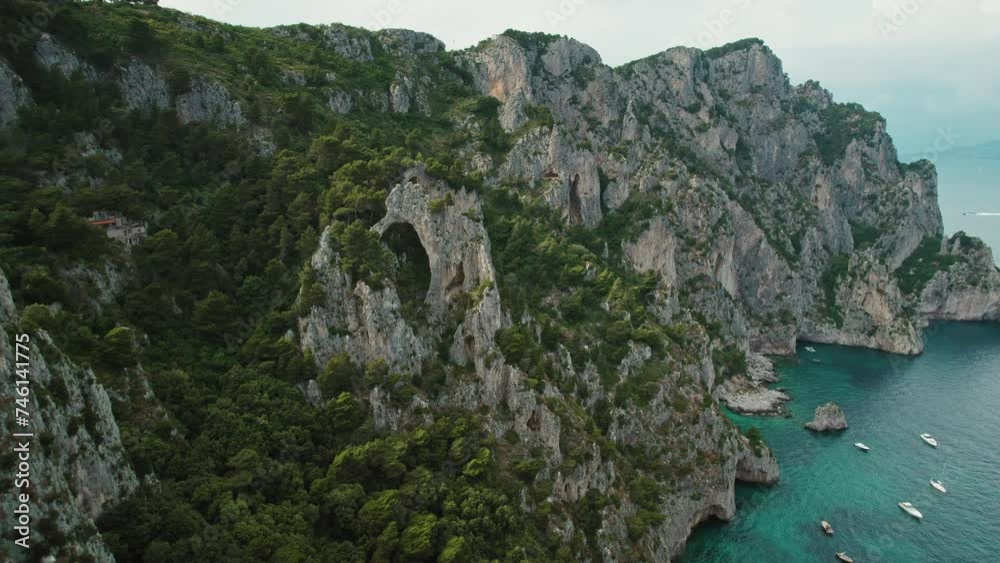 Cliffside arches of Capri overlook sea waters and anchored yachts. The natural arch formations and rugged coastline with maritime vessels on tranquil bay below. Cliffside arches of Capri overlook sea waters and anchored yachts. The natural arch formations and rugged coastline with maritime vessels on tranquil bay below.