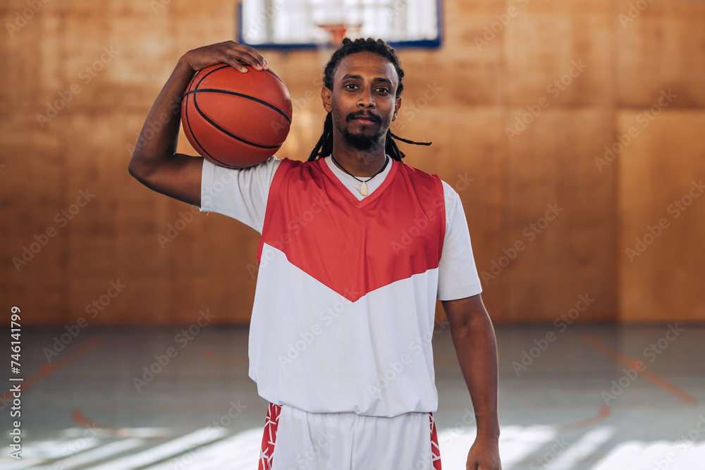 A muscular interracial basketball player is posing with a ball on court. A muscular interracial basketball player is posing with a ball on court.