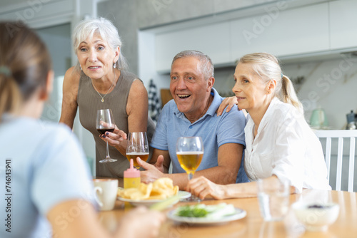 Joyous old men and women talking merrily while having snack with cold drinks in the kitchen