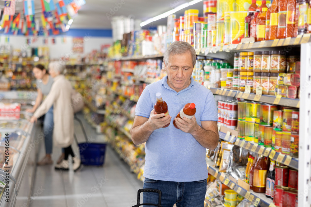 Attentive man purchaser choosing tomato juice out of large stock in a big supermarket