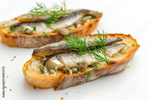 A close-up view of two slices of toasted bread topped with grilled sardines, and fresh dill, presented on a white background.