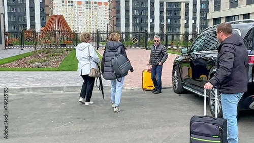 Parents and children take out heavy suitcases package from open trunk of black car on a street. Happy multi generations family is coming back home after road trip. Concept vacation, family travelling photo