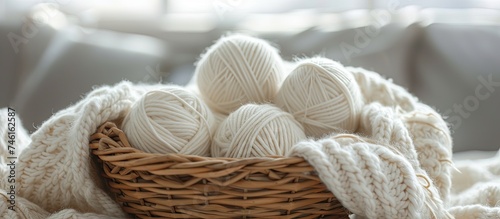 A wicker basket filled with white balls of yarn sits on top of a knitted blanket. The soft, fluffy yarn is neatly arranged within the basket, ready to be used for knitting or crocheting projects.