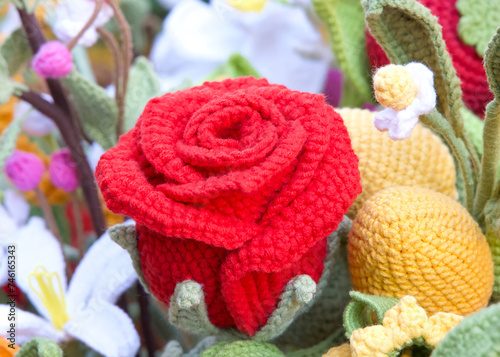 Close up on hand crafted crochet vibrant red rose flowers with a variety of spring color crochet flowers around them.