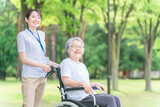 公園を散歩する車椅子の高齢者と介護士・看護師・理学療法士・運動指導員の女性 