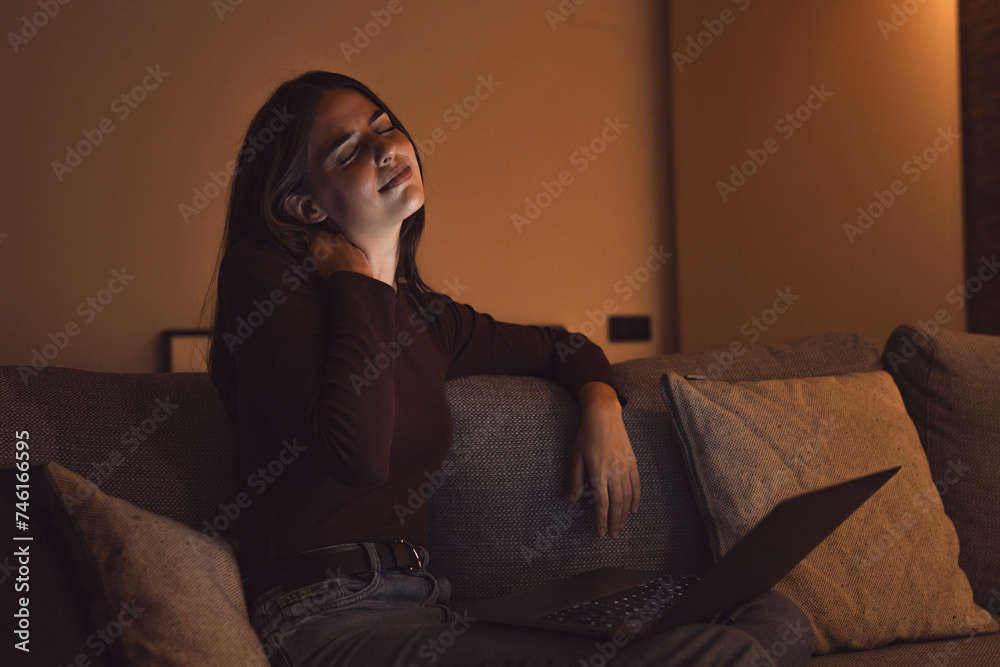 Stressed woman at late night having strong terrible neckache attack after computer laptop study, sleepy exhausted girl suffering from chronic migraine massaging muscle to relieve neck ache tension.