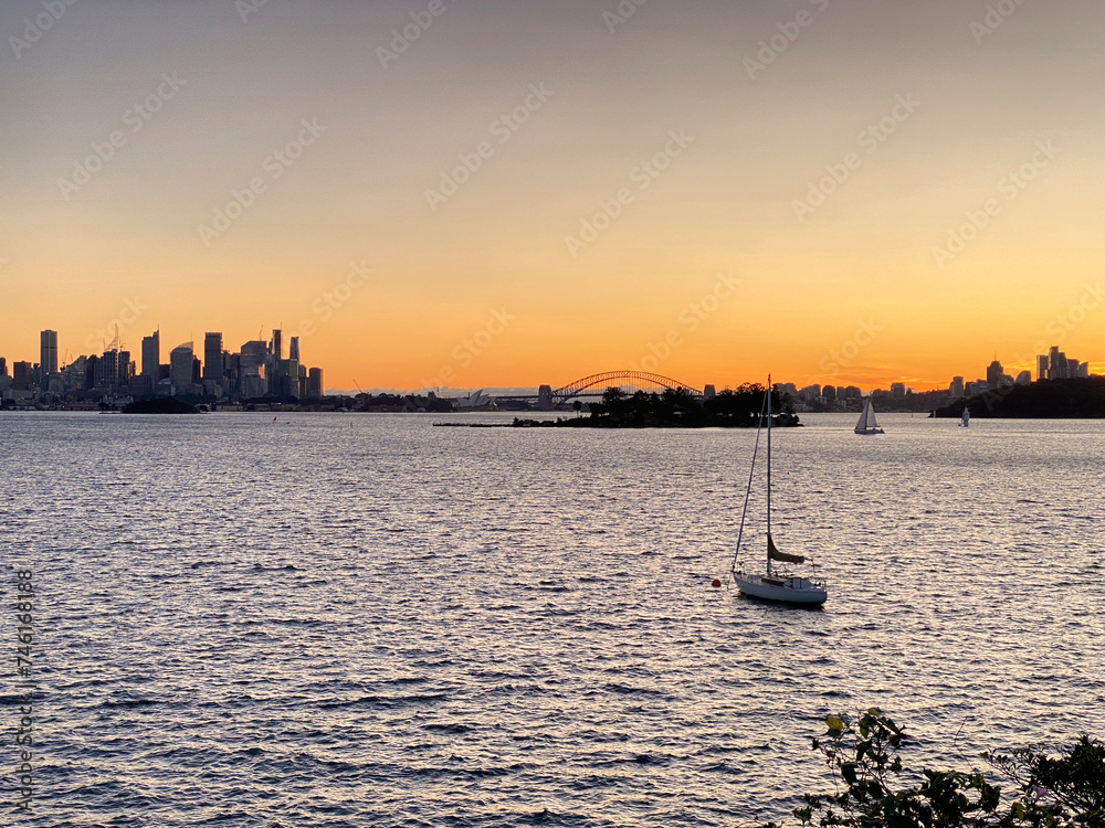 Sunset over the river. Boats in the bay. Town on the horizon from the ocean shore. Recreational yachts in the water at dusk. Sailboat with masts anchored in the bay at sundown.