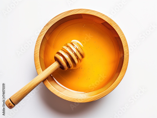 A wooden bowl overflows with golden honey, with a dipper, against a pristine white background, seen from above.