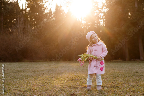girl 5 years old in a pink coat and hat in retro style with a bouquet of pink tulips in early spring in the park in backlit sunlight. photo