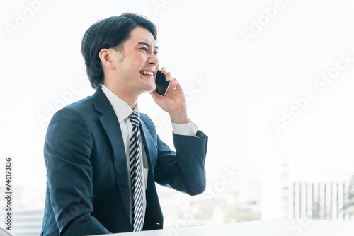 オフィスでスマホを使う若いアジア人ビジネスマン（電話・営業・アポ・営業活動）
