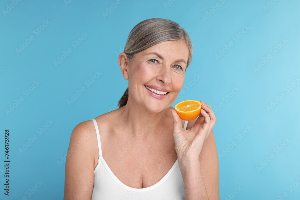 Beautiful woman with half of orange rich in vitamin C on light blue background Beautiful woman with half of orange rich in vitamin C on light blue background