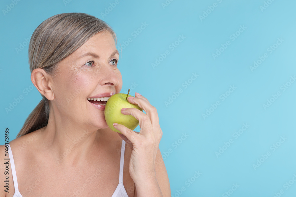 Beautiful woman eating fresh apple on light blue background, space for text. Vitamin rich food Beautiful woman eating fresh apple on light blue background, space for text. Vitamin rich food