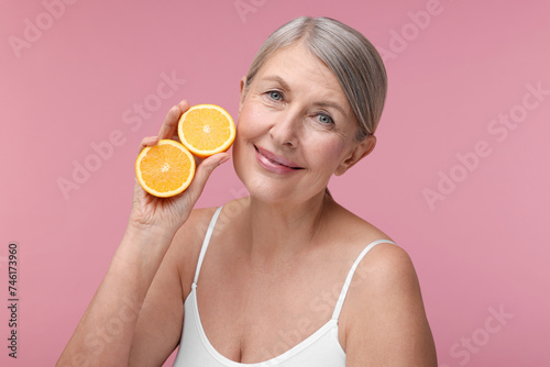 Beautiful woman with halves of orange rich in vitamin C on pink background