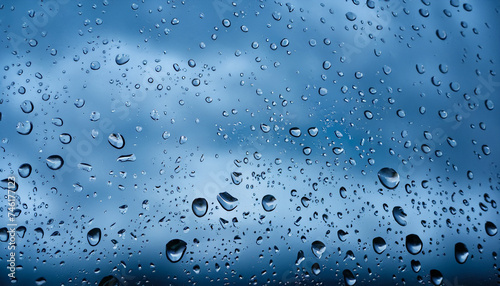 Water drops on a glass pane in front of dark rain clouds in blue colors; abstract background; vertical, closeup shot