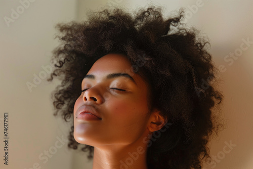 Portrait of a young woman with her eyes closed, basking in a warm light, showcasing her natural curly hair.