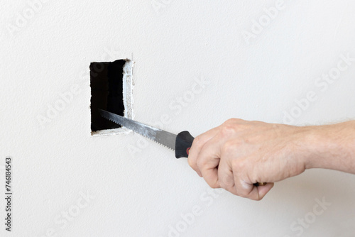 Cutting hole in the drywall. Electrician using drywall knife to cut a hole photo