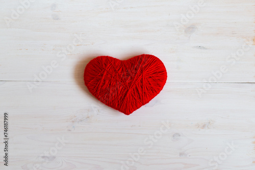 Red heart shape made from wool on white wooden background
