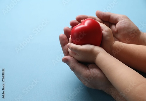 Fototapeta Naklejka Na Ścianę i Meble -  Father and his child holding red decorative heart on light blue background, closeup. Space for text