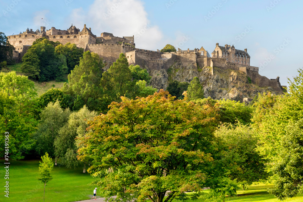 Edinburgh, Scotland - Edinburgh Castle, perched on its rock above the trees on Princes Street Gardens. Jogger going by.
